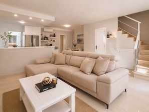 A modern living room with a beige sectional sofa, a white coffee table, and a staircase.