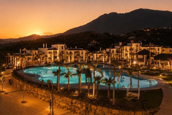 A resort with a large swimming pool, palm trees, and a mountain backdrop.