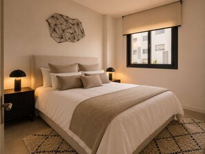 Ein Schlafzimmer mit einem großen Bett, zwei Nachttischen mit Lampen, einer geometrischen Wanddekoration, einem Fenster mit Ausblick und einem gemusterten Teppich.
