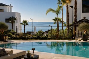 Ein Pool mit Blick auf das Meer, Palmen und ein Gebäude mit heller Fassade.