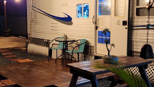 A covered outdoor area with a dining table and chairs, a small garden, and a white RV parked in the background. - Camper Capacidad Hasta 6 Personas (Cabo Rojo)