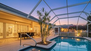 Un área de piscina moderna al aire libre con zona de estar cubierta y una chimenea.