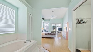 Un baño con bañera, ducha e inodoro. Un pasillo conduce a un dormitorio con cama y cómoda.