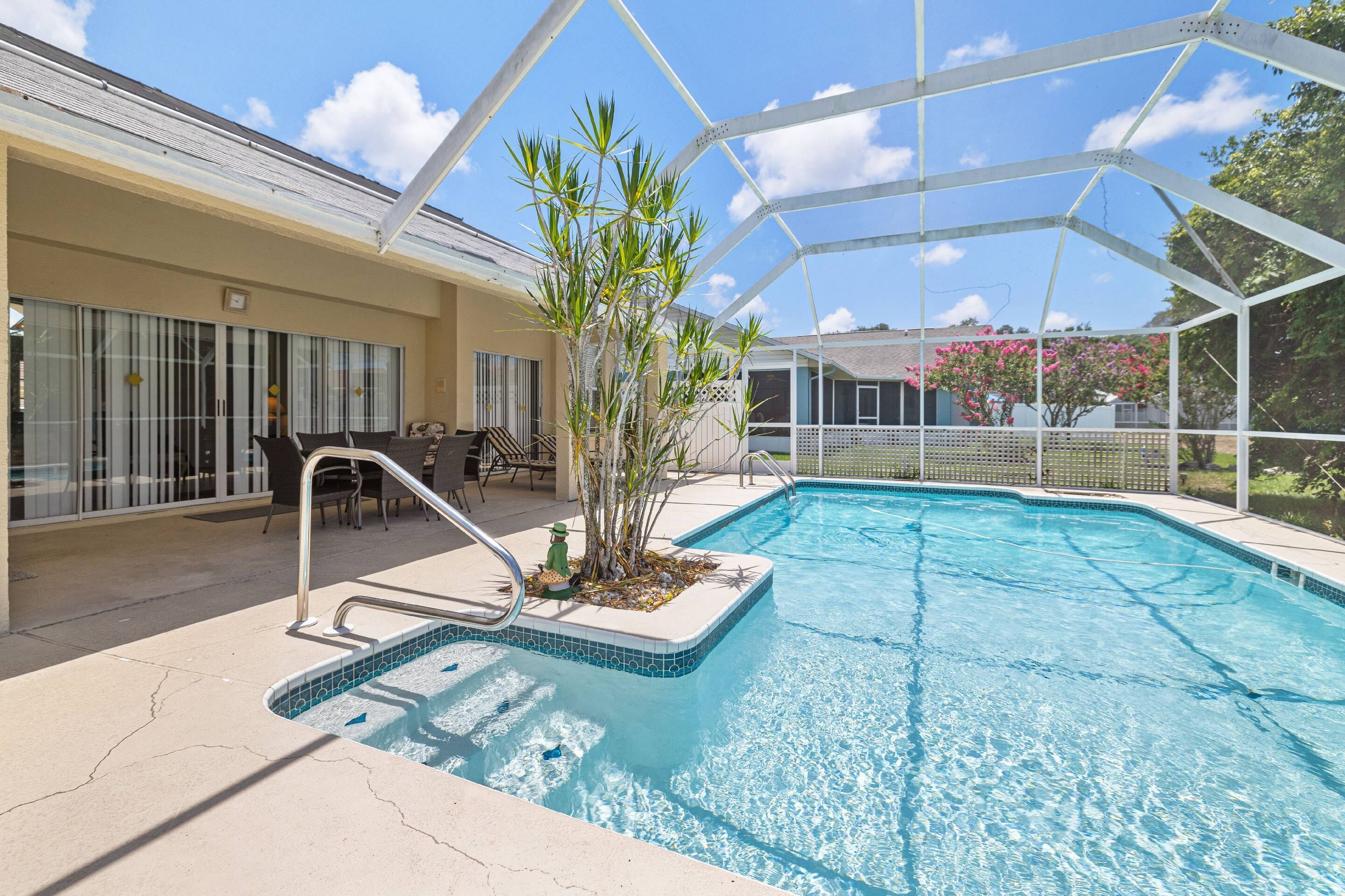 A swimming pool with a covered area, a patio with chairs, and a view of the surrounding landscape.