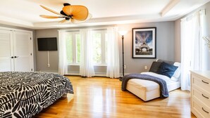 A bedroom with a bed, a sofa, a desk, a lamp, a painting of the Eiffel Tower, and a ceiling fan. - Mins to Downtown in Waterfront community at Pet-Friendly Pinecrest Bungalow (Annapolis)