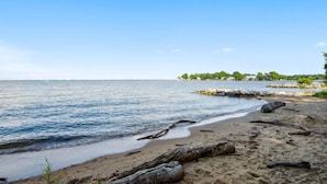 A beach with clear water, a sandy shore, and a distant shoreline with buildings and greenery. - Mins to Downtown in Waterfront community at Pet-Friendly Pinecrest Bungalow (Annapolis)