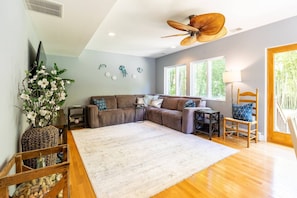 A living room with a brown sofa, a white rug, a wooden coffee table, and a ceiling fan.