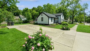 Ein zweistöckiges Haus mit Vorgarten, Auffahrt und einem kleinen Garten mit rosa Blumen.