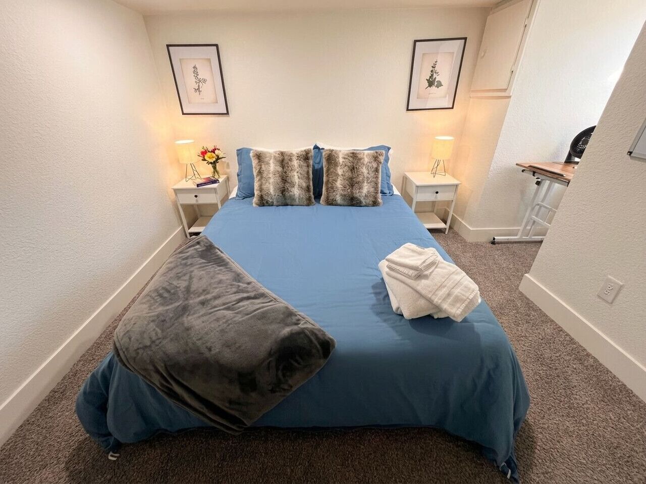 A bedroom with a bed, pillows, a bedside table with a lamp, and a wall-mounted picture.