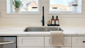A kitchen with white cabinets, a stainless steel sink, and two windows. - Huge 6BR Highlands Home - Modern Style & Comfort (Denver)