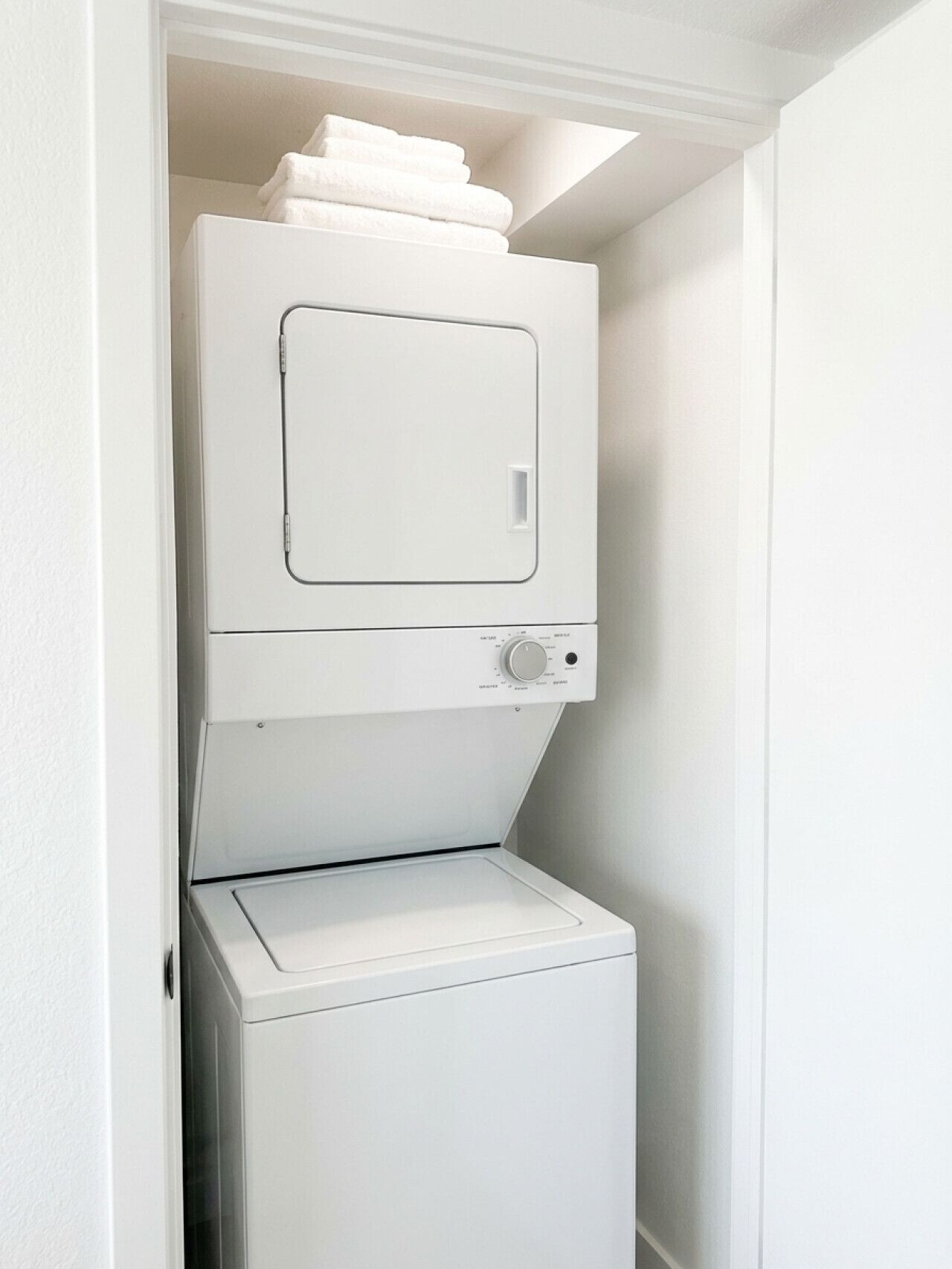 A compact laundry room with a stacked washer and dryer, a small window above the dryer, and a white door.