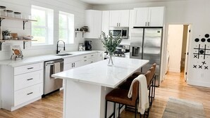 A modern kitchen with white cabinetry, a marble island, and a seating area with a plant. - Huge 6BR Highlands Home - Modern Style & Comfort (Denver)