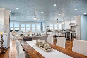 A spacious living area with a wooden dining table, a sofa, and a view of the ocean through large windows.