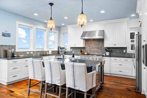A modern kitchen with white cabinetry, a central island with bar stools, a stainless steel stove, and pendant lighting.