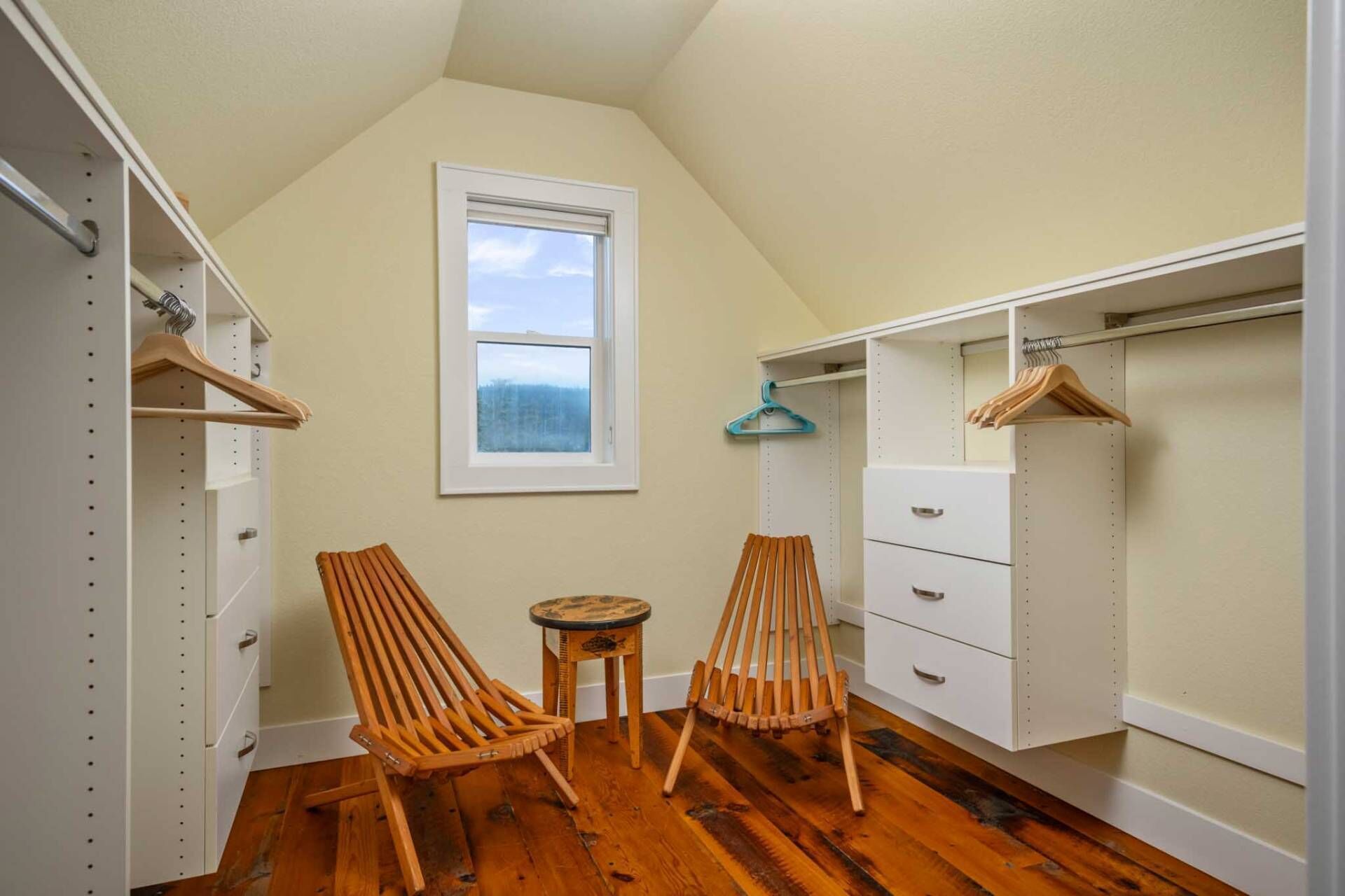 A small, well-lit closet with wooden chairs, a small table, and a window providing a view of the outdoors.