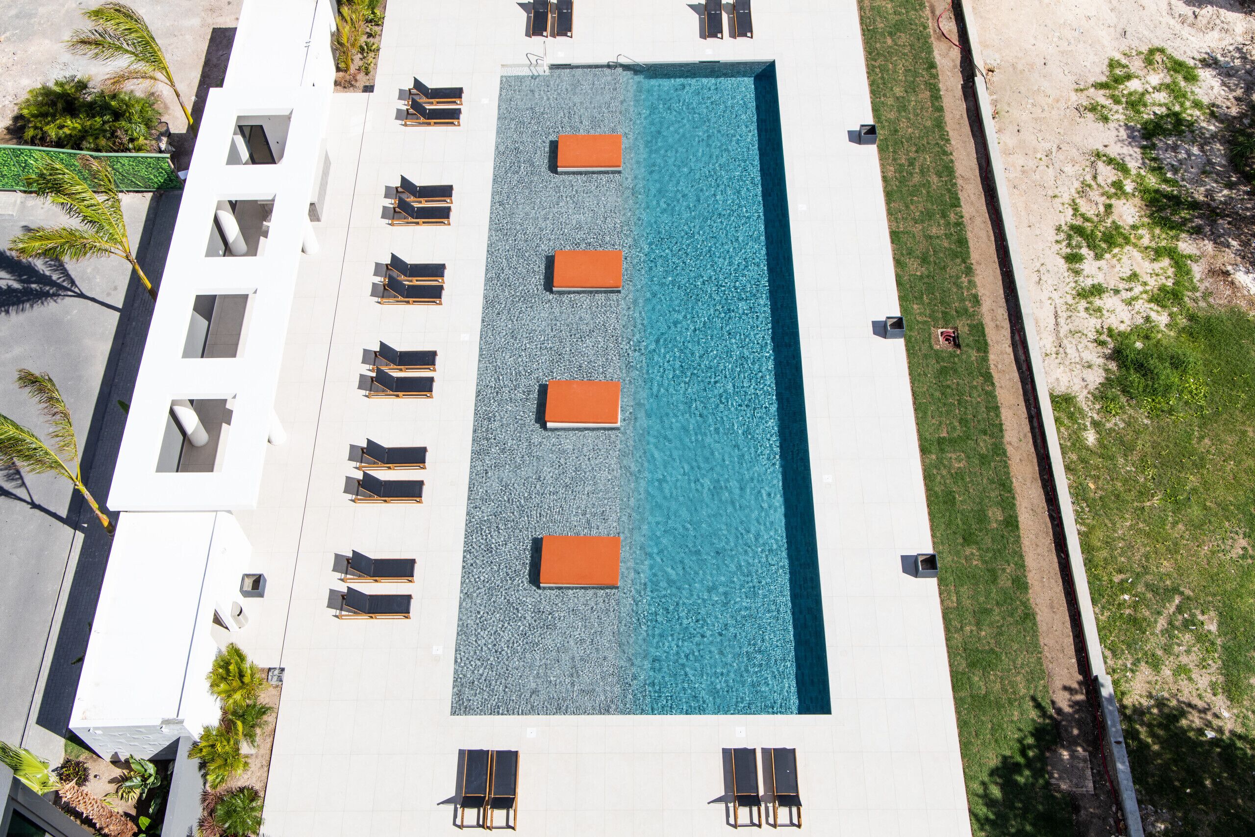 An aerial view of a hotel with a rectangular pool, multiple lounge chairs, and a white building facade.
