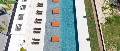 Vista aérea de um hotel com piscina retangular, várias espreguiçadeiras e fachada de prédio branca.