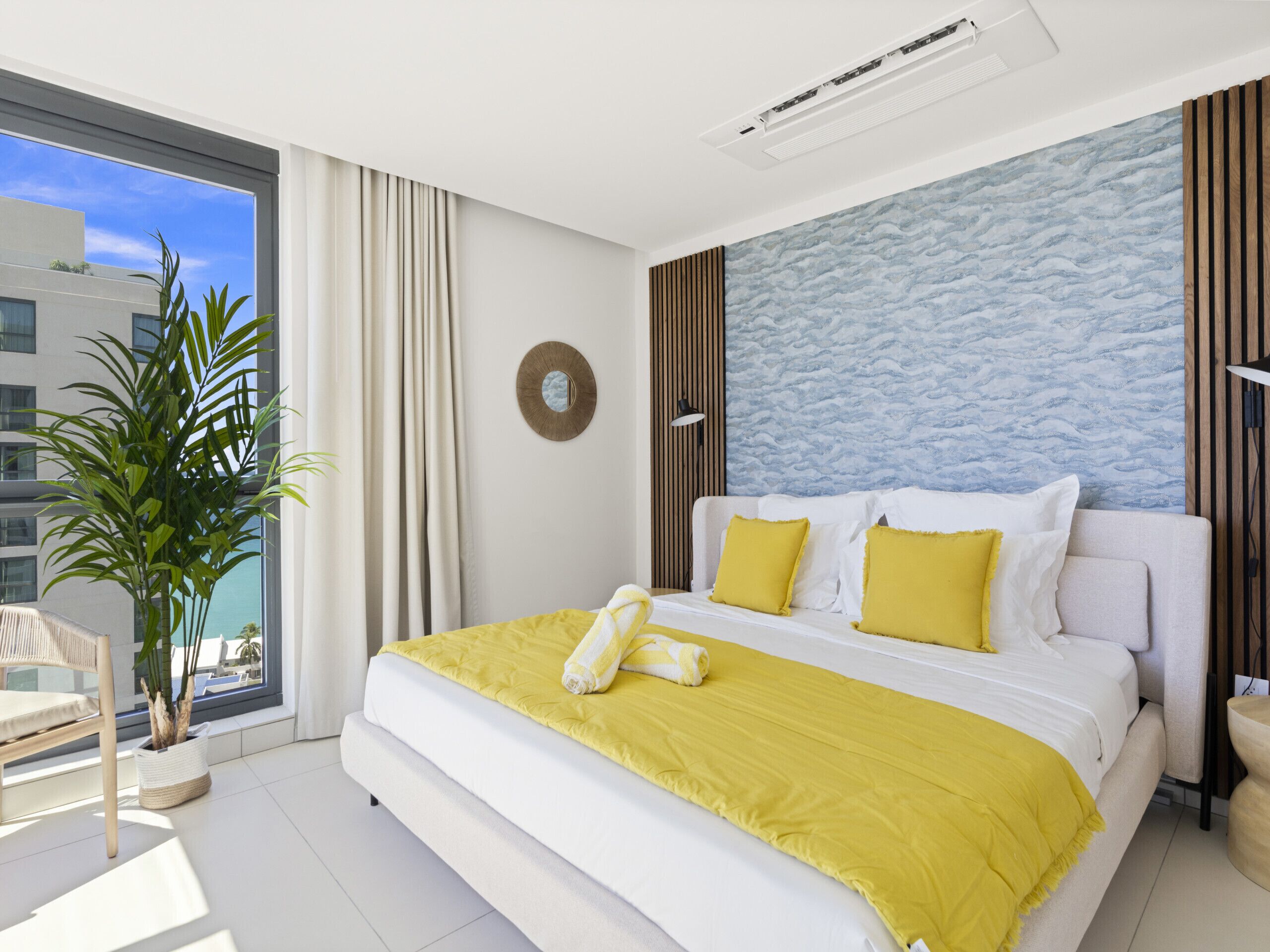 Ein modernes Schlafzimmer mit einem großen Bett, Blick auf die Stadt und einer Zimmerpflanze.