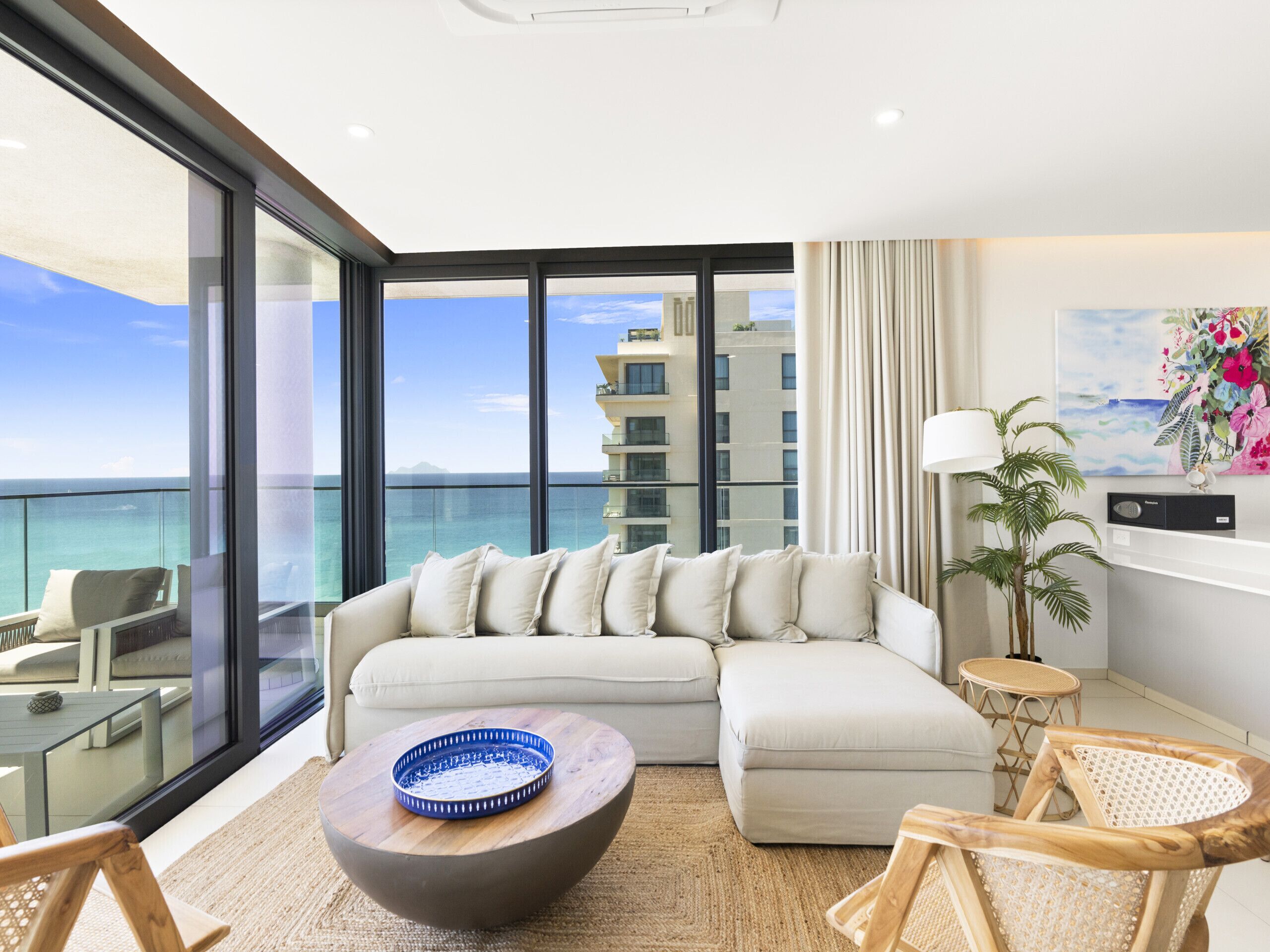 A modern living room with a large window, a sofa, a coffee table, and a view of the ocean.
