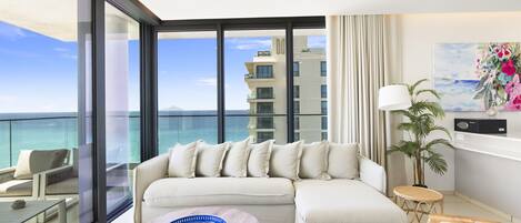 A modern living room with a large window, a sofa, a coffee table, and a view of the ocean.