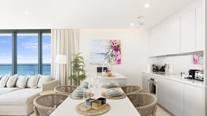 Ein modernes Wohnzimmer mit einem weißen Sofa, einem Esstisch mit Gläsern und Blick auf den Ozean.