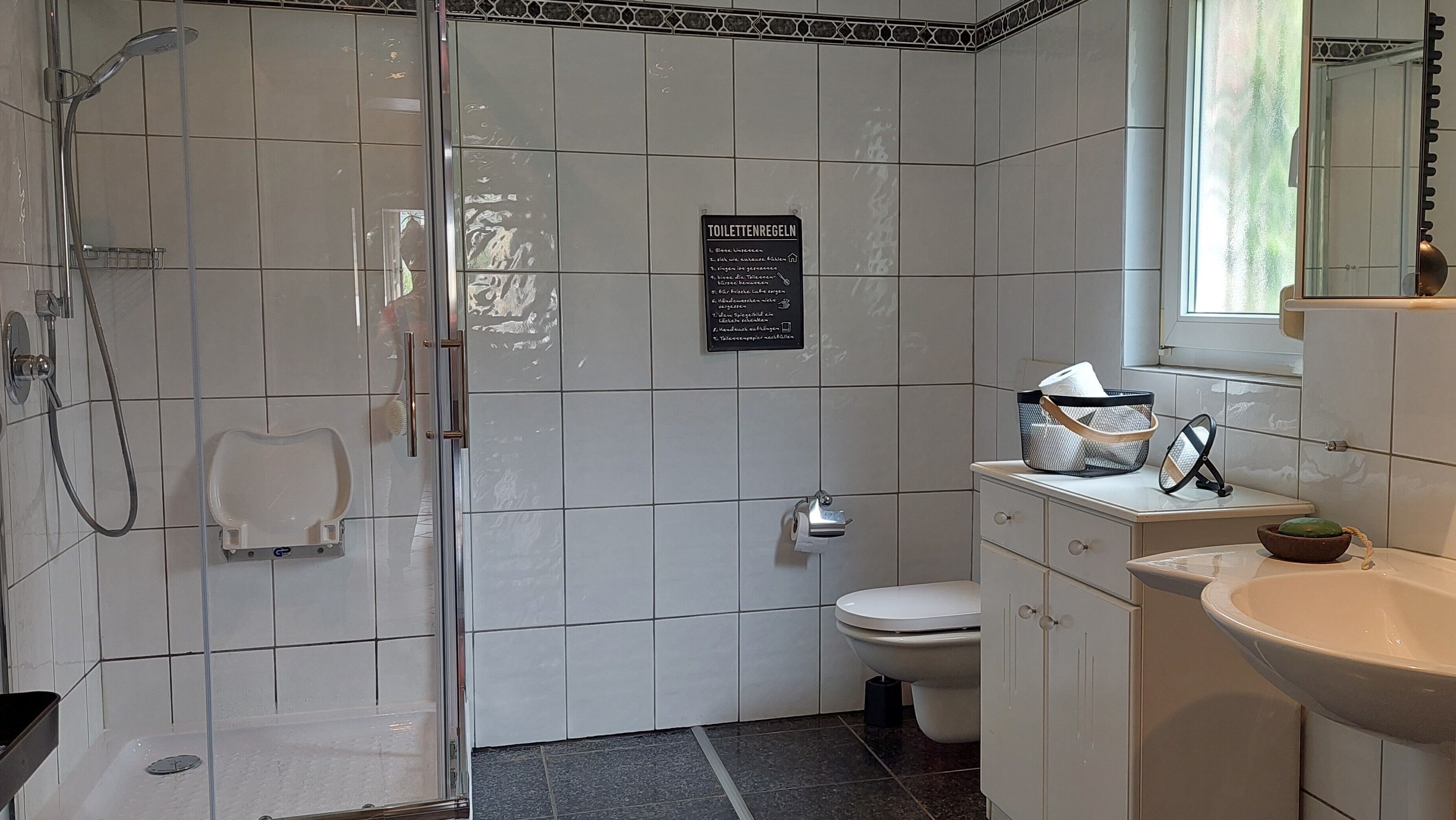 Ein Badezimmer mit Dusche, Toilette, Waschbecken und einem Schild mit Regeln.