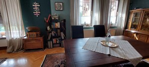 A dining area with a wooden table, chairs, a buffet tray, a bookshelf, and a window with curtains.