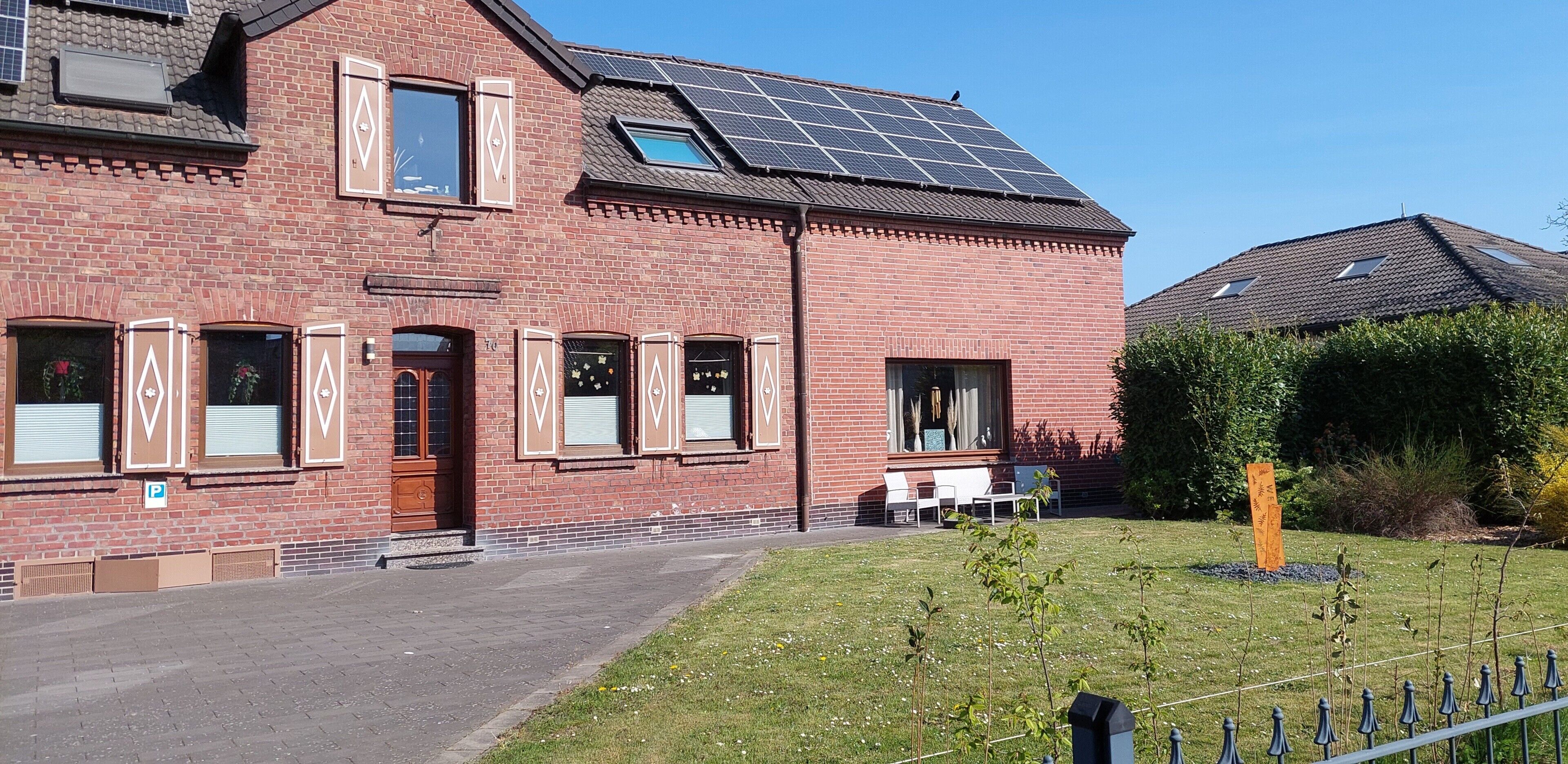 Ein Gebäude aus Ziegelsteinen mit einer Solaranlage auf dem Dach, einem kleinen Garten und einem Zaun.