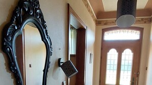 Un pasillo con un espejo grande y ornamentado, una puerta con paneles de vidrio y una lámpara en el techo.