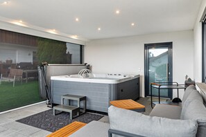 A modern living room with a hot tub, a sofa, a small table, and a glass door leading to a balcony. - Apartment 'Fewo Wegen' with Mountain View, Private Terrace & Wi-Fi (Salem)