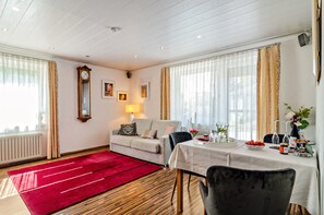 A hotel room with a red carpet, a sofa, a dining table set with a vase, and a clock on the wall. - Apartment 'Fewo Wegen' with Mountain View, Private Terrace & Wi-Fi (Salem)