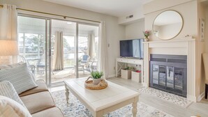 A living room with a sofa, coffee table, TV, fireplace, and a sliding glass door leading to a balcony. - Porch & Water Views: Getaway in Mallard Lakes (Selbyville)