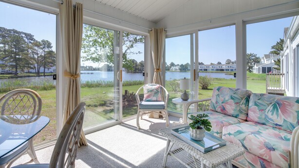 A sunlit room with a view of a lake, featuring a sofa, chairs, and a table. - Porch & Water Views: Getaway in Mallard Lakes (Selbyville)