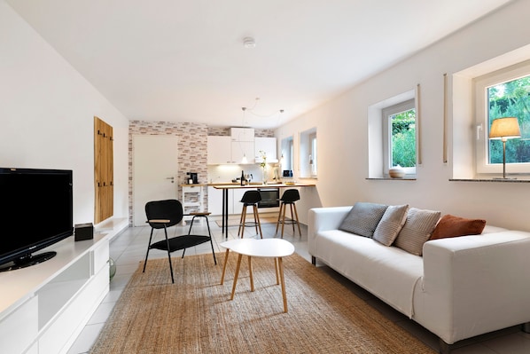 A modern living room with a flat-screen TV, a white sofa, and a dining area with chairs and a table. - Studio Apartment 'Ferienwohnung Vino9' with Private Garden and Wi-Fi (Vogtsburg im Kaiserstuhl)