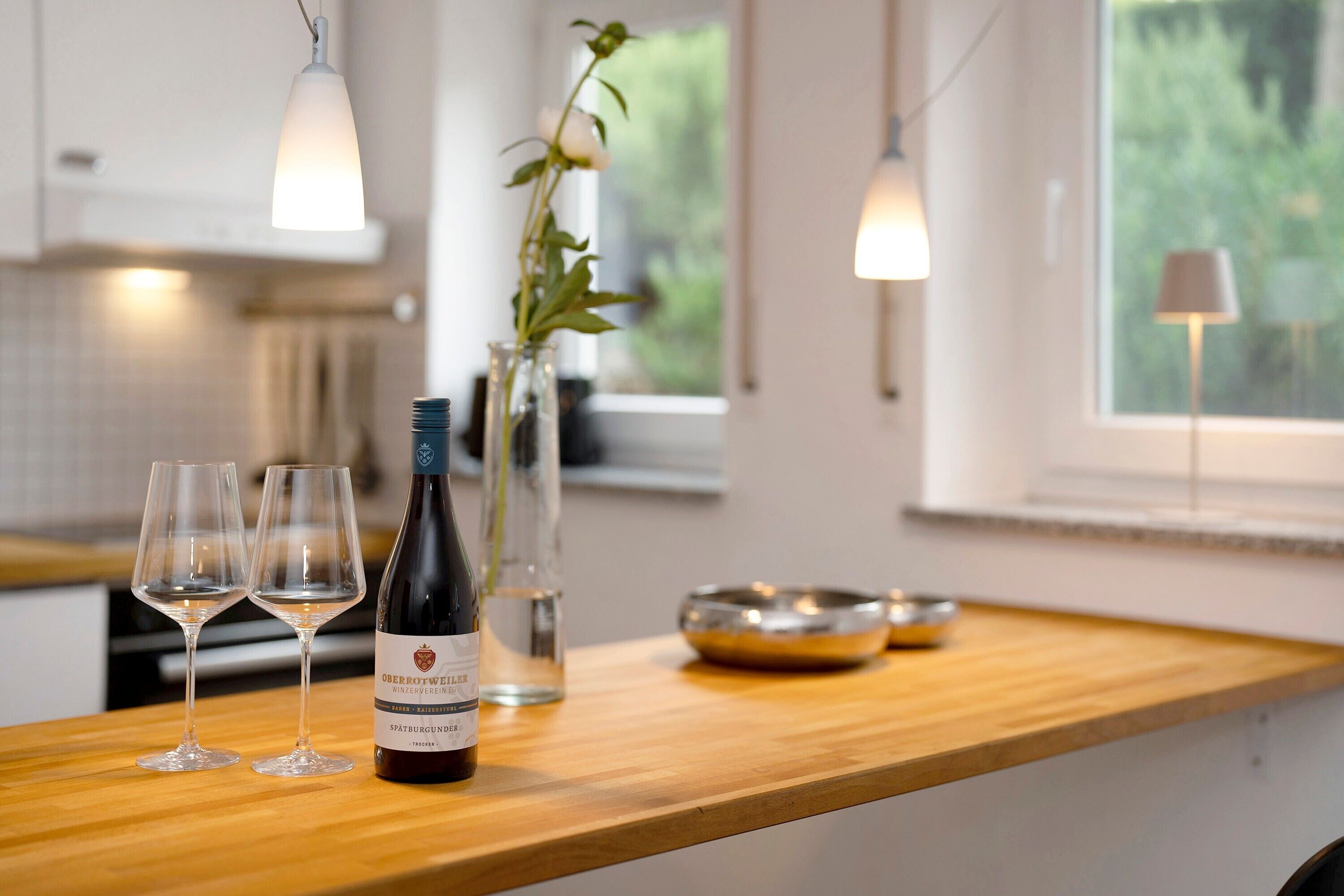 A kitchen counter with wine glasses, a bottle, and a vase with a plant.