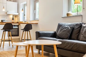 A modern living room with a leather sofa, two chairs, a small table, and a kitchen in the background.