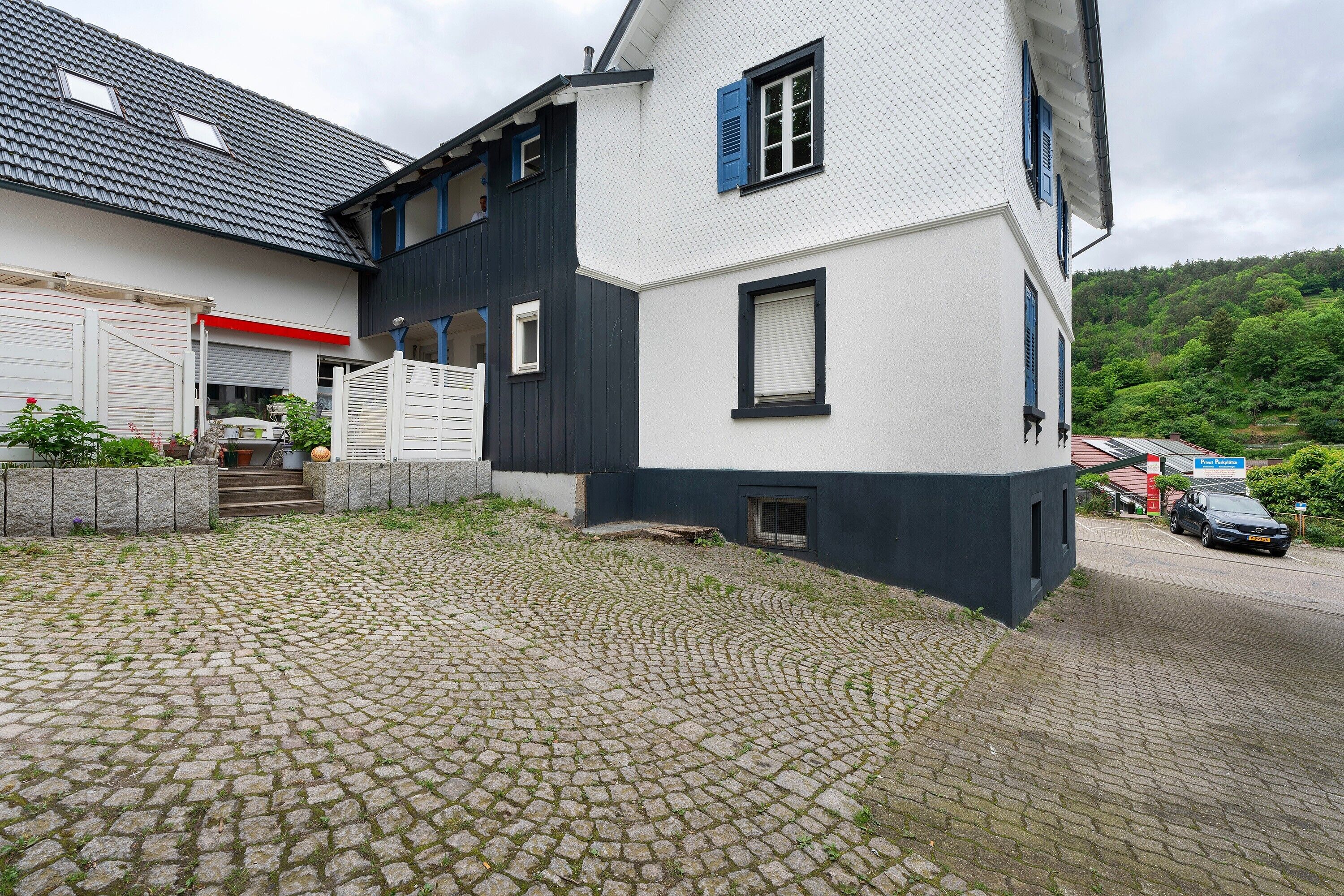 Een gebouw met twee verdiepingen, een keienpad, een garage en uitzicht op een weelderige groene heuvel.