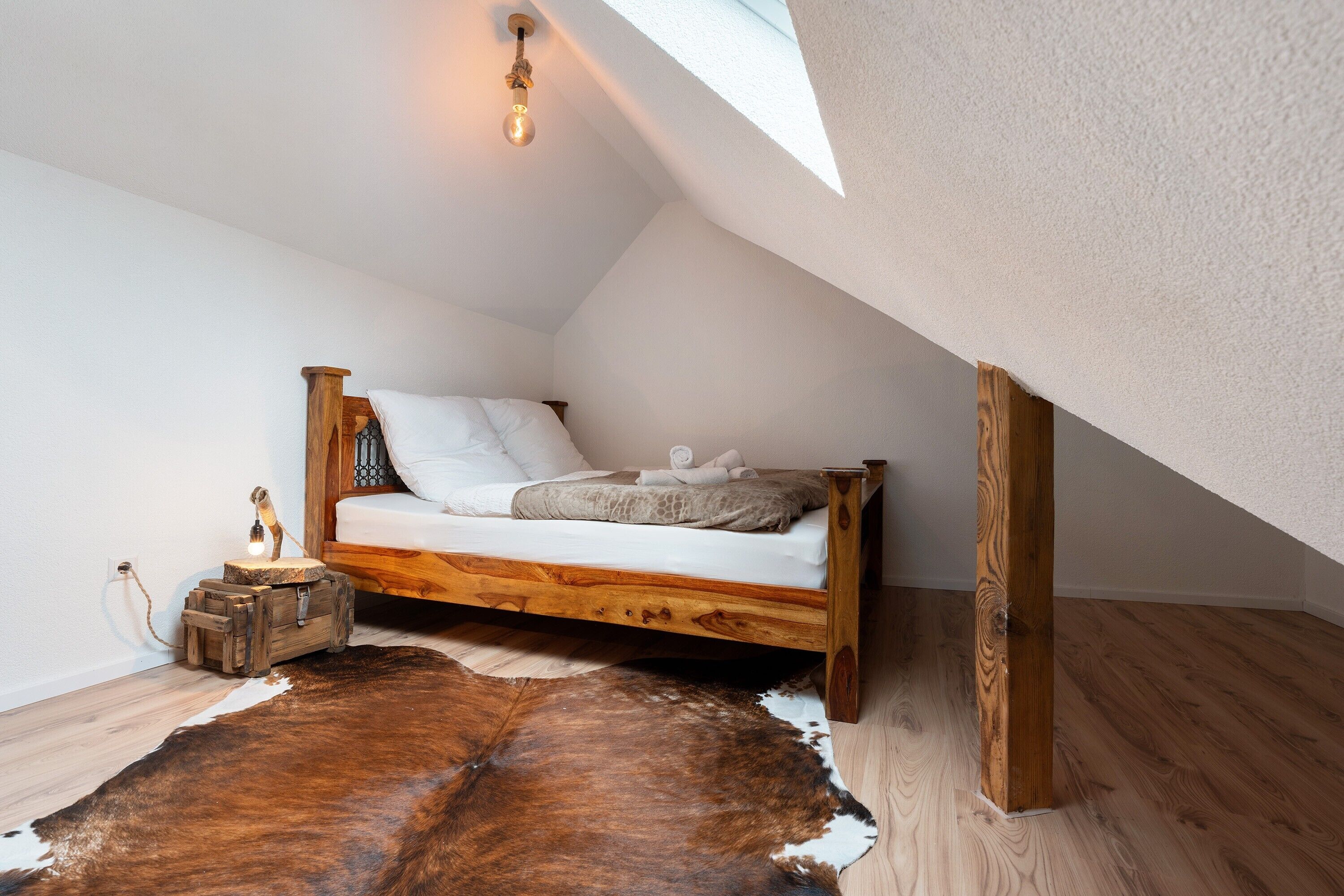 A loft bedroom with a wooden bed, a cowhide rug, a small wooden chest, and a skylight.