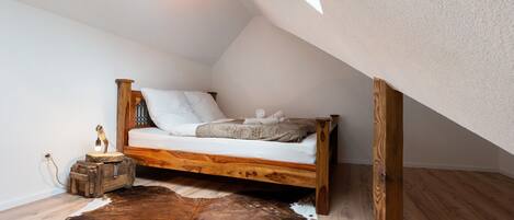 A loft bedroom with a wooden bed, a cowhide rug, a small wooden chest, and a skylight.