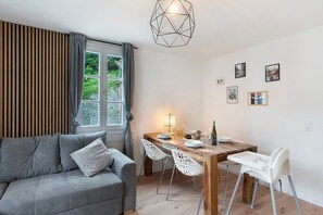 Ein modernes Wohnzimmer mit einem grauen Sofa, einem Holzesstisch mit Stühlen und einer geometrischen Pendelleuchte.