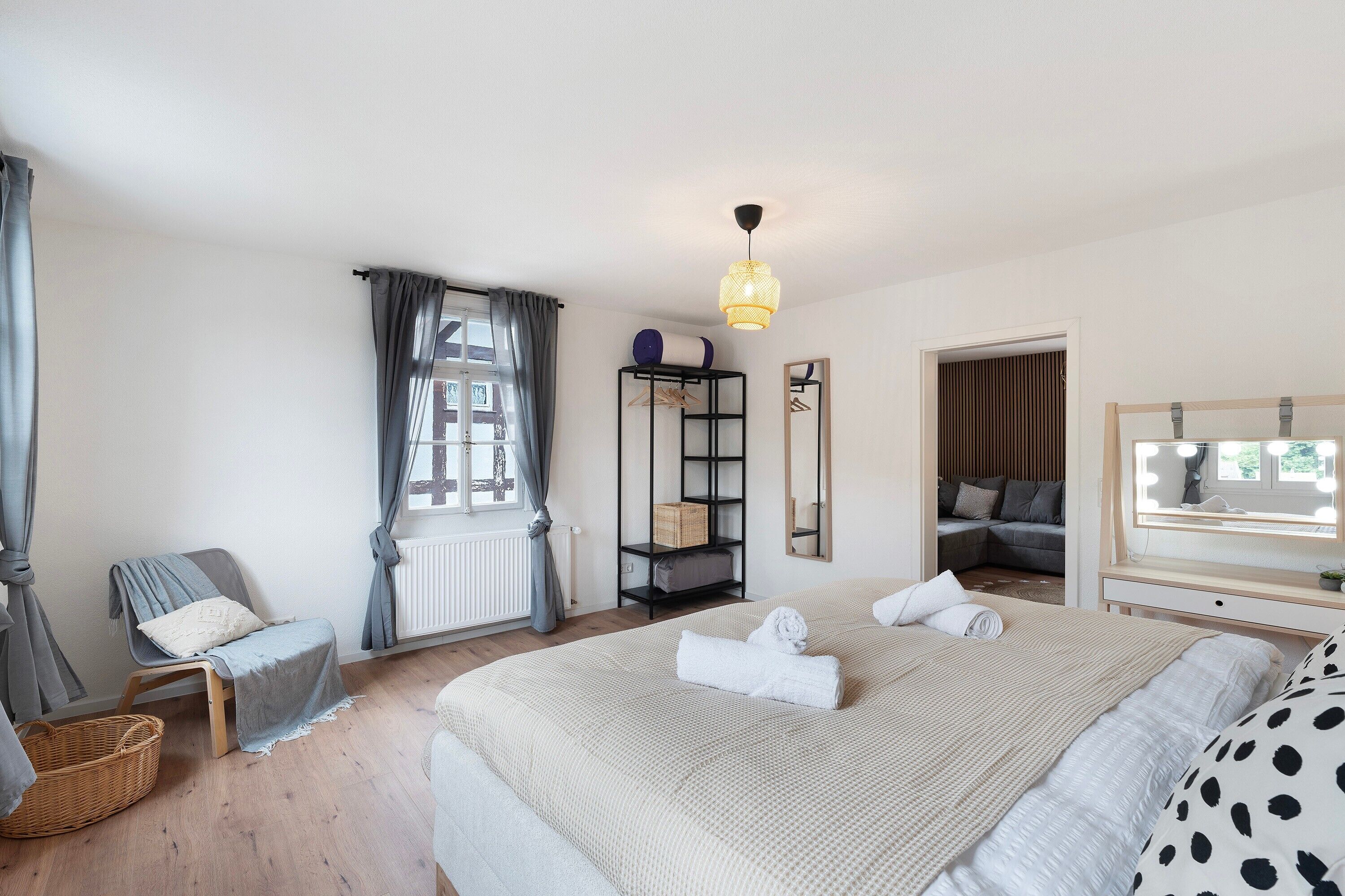 A bedroom with a large bed, a chair, a small table, a wardrobe, and a window with curtains.