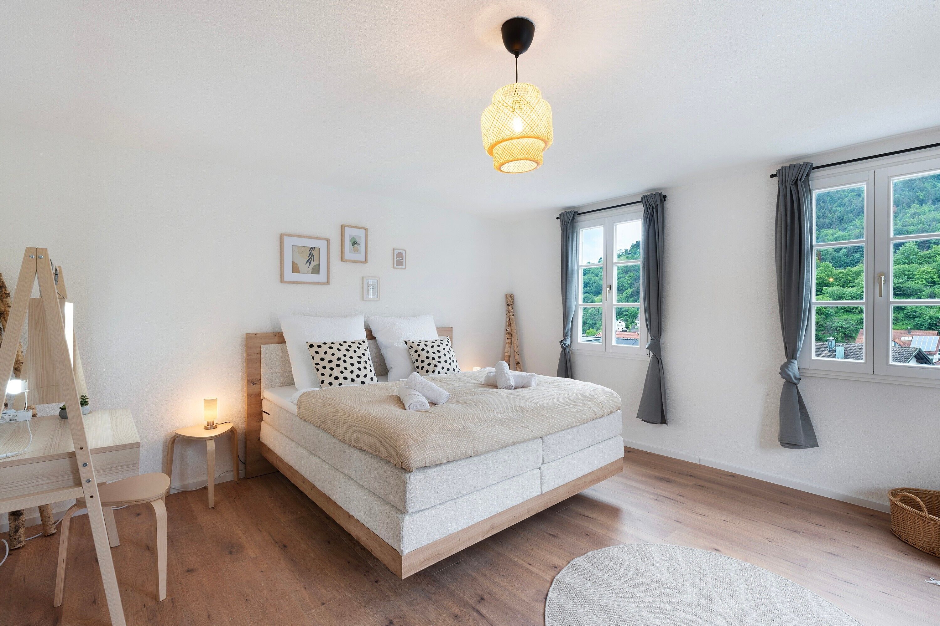 Une chambre à coucher avec un lit, une table de chevet, une lampe et une vue sur la verdure à l’extérieur.