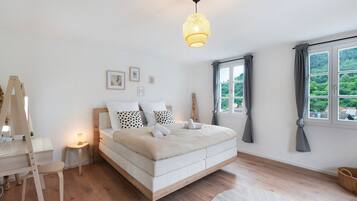 Une chambre à coucher avec un lit, une table de chevet, une lampe et une vue sur la verdure à l’extérieur.