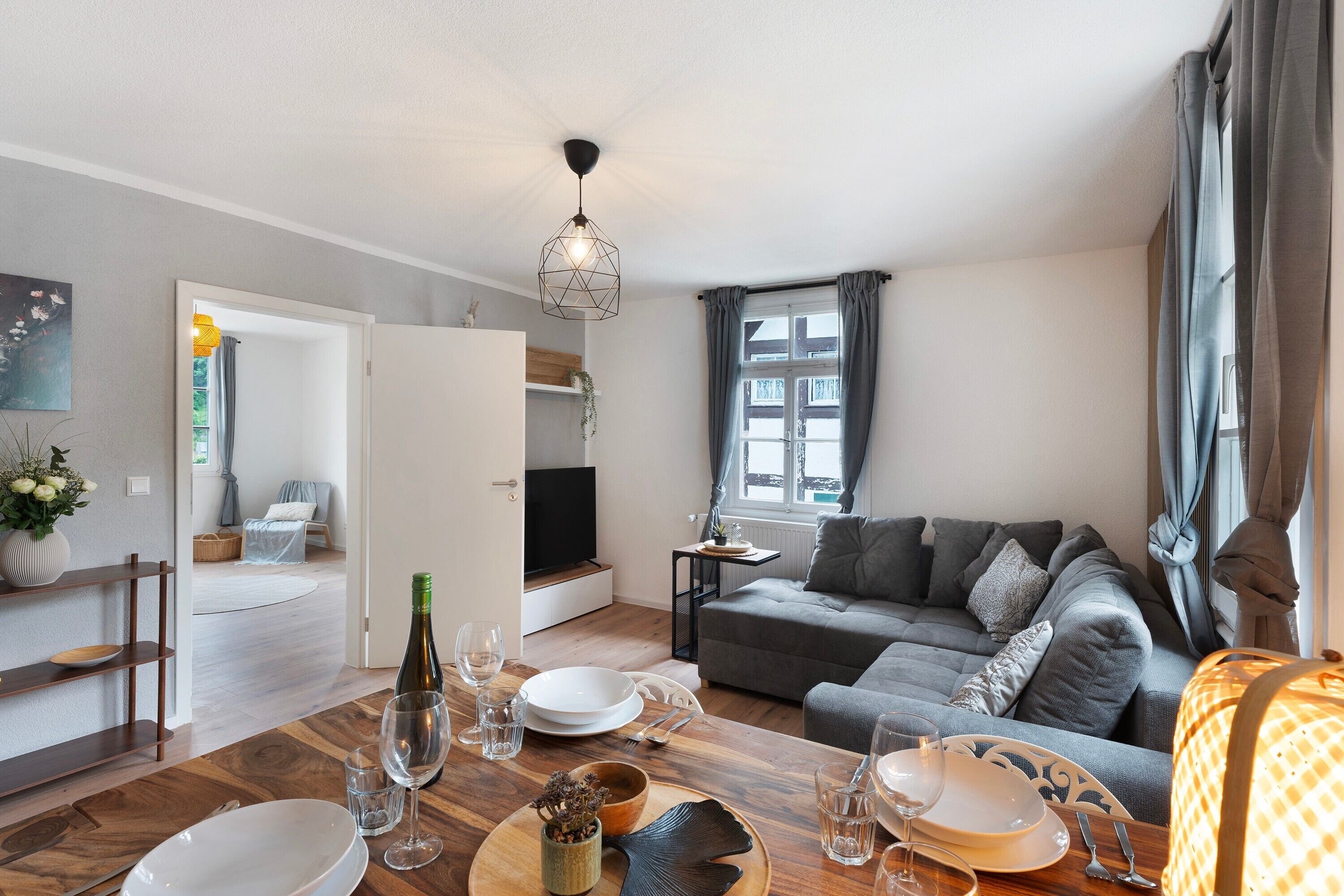 A modern living room with a dining area, grey sofa, and a TV.