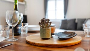 A dining table with a bottle of wine, a glass, a small plant, and a wooden cutting board. - Apartment 'Appartement Waldblick' with Mountain View, Shared Garden and Wi-Fi (Bühlertal)