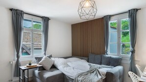 A modern bedroom with a bed, a side table, a radiator, and a window with curtains. - Apartment 'Appartement Waldblick' with Mountain View, Shared Garden and Wi-Fi (Bühlertal)