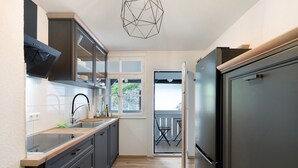 A modern kitchen with a built-in oven, a stainless steel refrigerator, and a window overlooking a balcony. - Apartment 'Appartement Waldblick' with Mountain View, Shared Garden and Wi-Fi (Bühlertal)