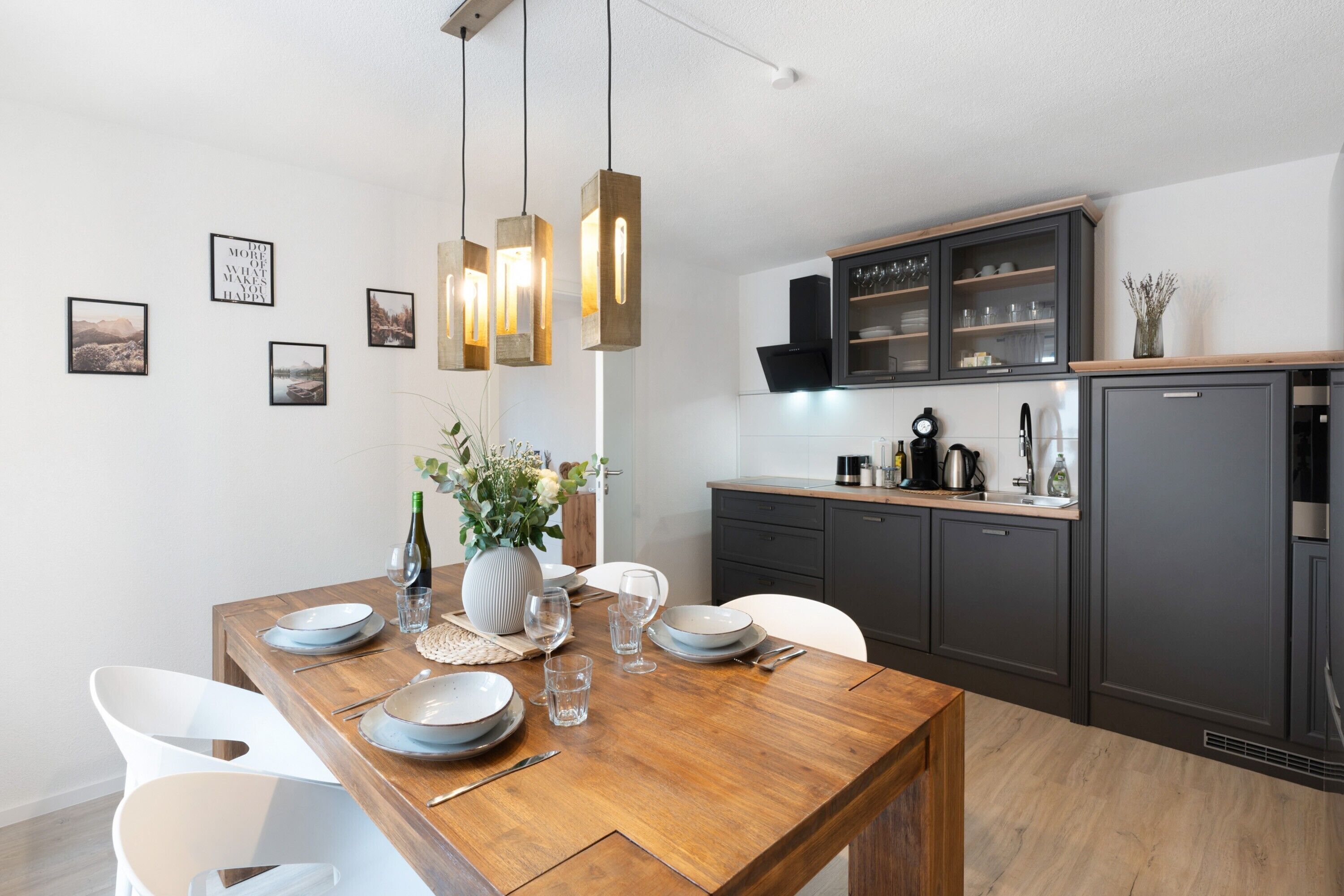 Een moderne keuken met een houten eettafel, witte stoelen en hanglampen.