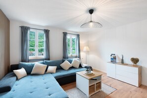 A modern living room with a sectional sofa, a small side table, a white cabinet, and a ceiling light fixture.