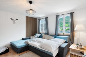 A modern bedroom with a bed, bedside tables, a lamp, and a view of greenery outside.